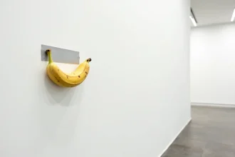 Une banane fixée avec du ruban adhésif argenté sur un mur blanc de galerie d'art contemporain, œuvre conceptuelle minimaliste.